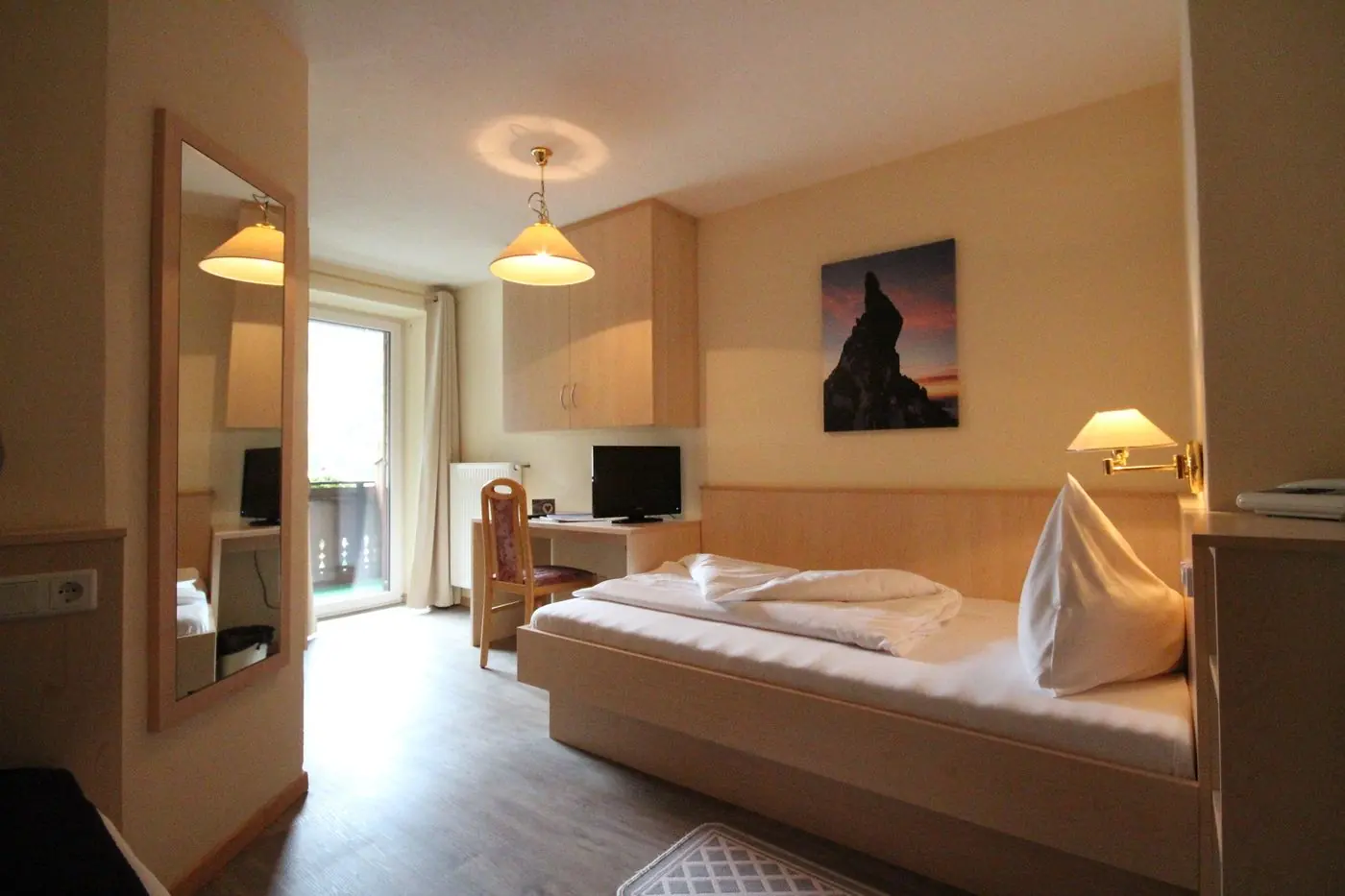 Einzelzimmer mit Schreibtisch, Fernseher und Balkontür